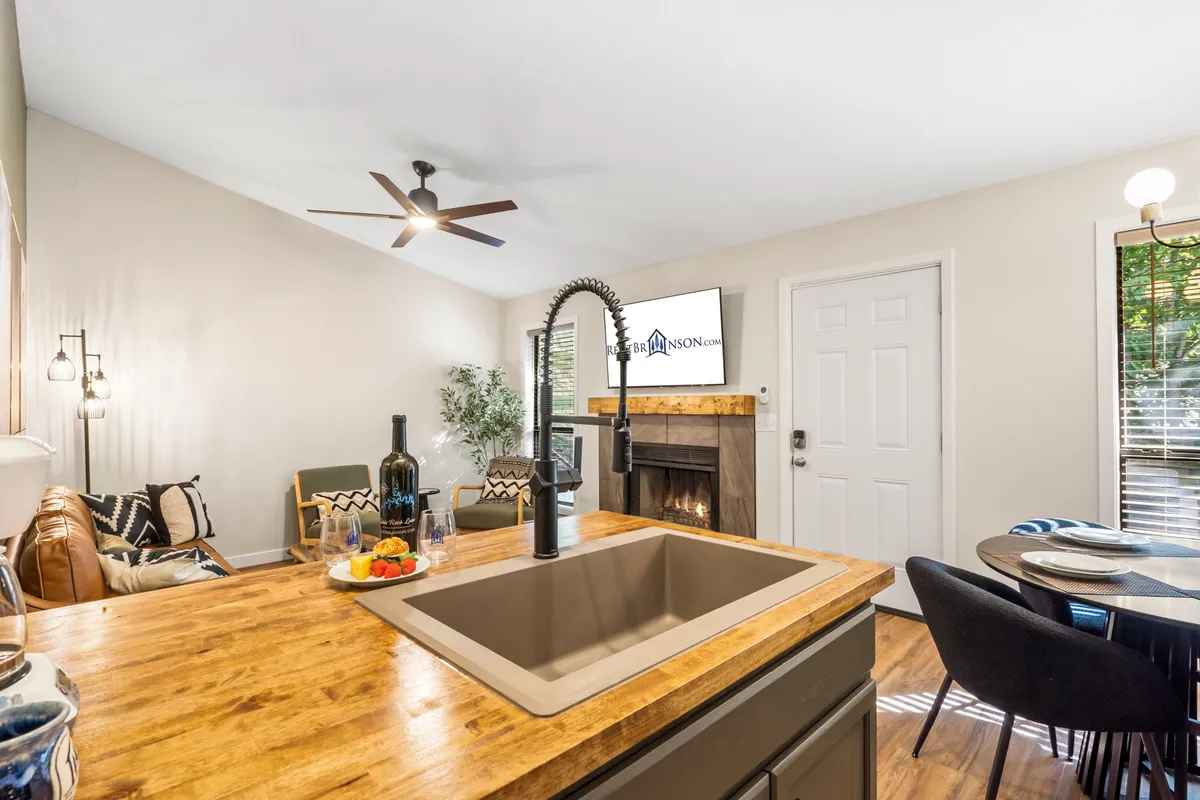 This image shows an inviting open-concept space seamlessly blending the kitchen, dining area, cozy fireplace, and a comfortable seating area, all bathed in natural light. Modern furnishings and warm details encourage gatherings, relaxation, and shared meals.