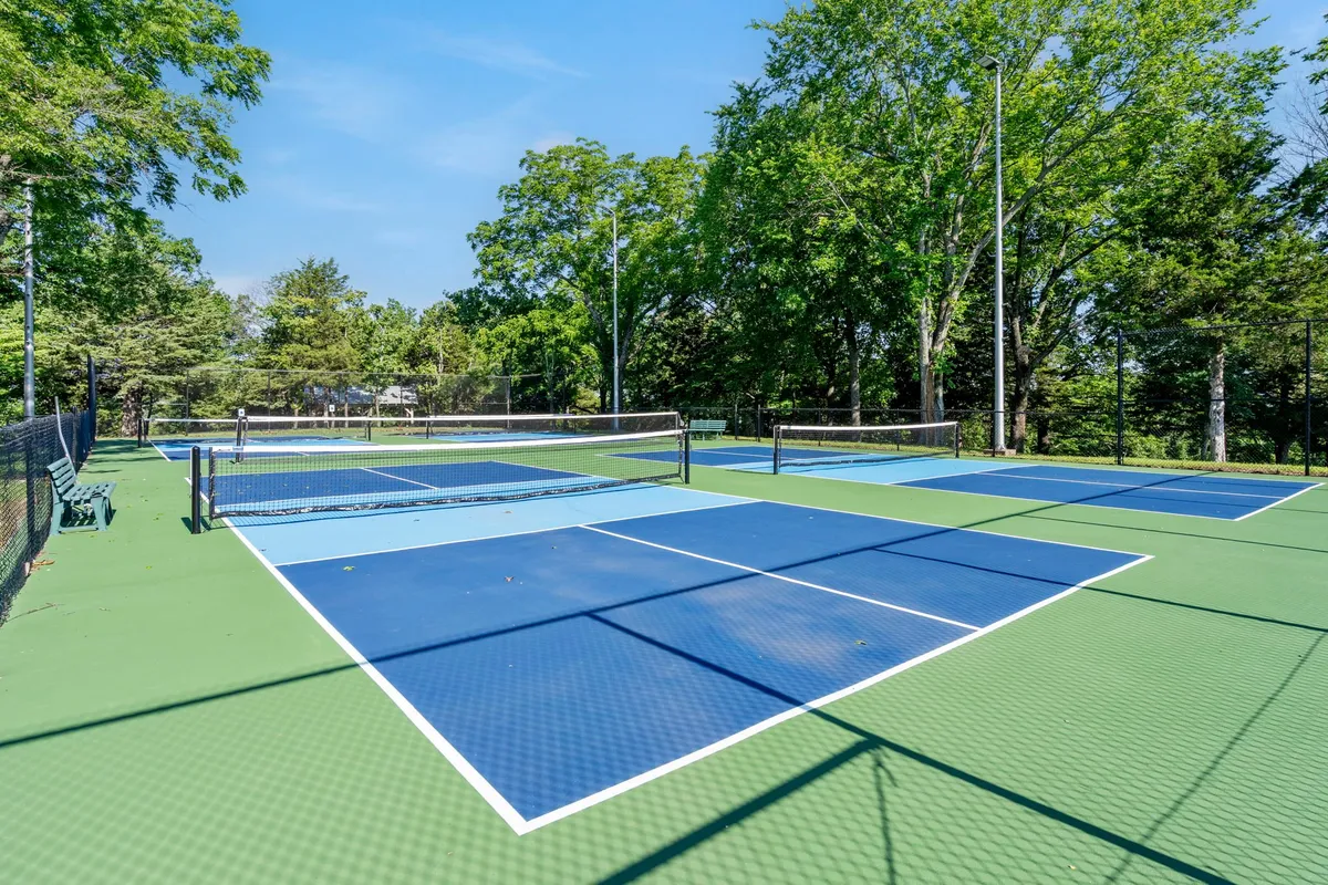 This exterior scene features well-maintained tennis (or multi-use sports) courts with people actively playing, set against a backdrop of green surroundings and blue sky. The energetic mood and communal activity spotlight the year-round opportunities for sports and socializing at the resort.