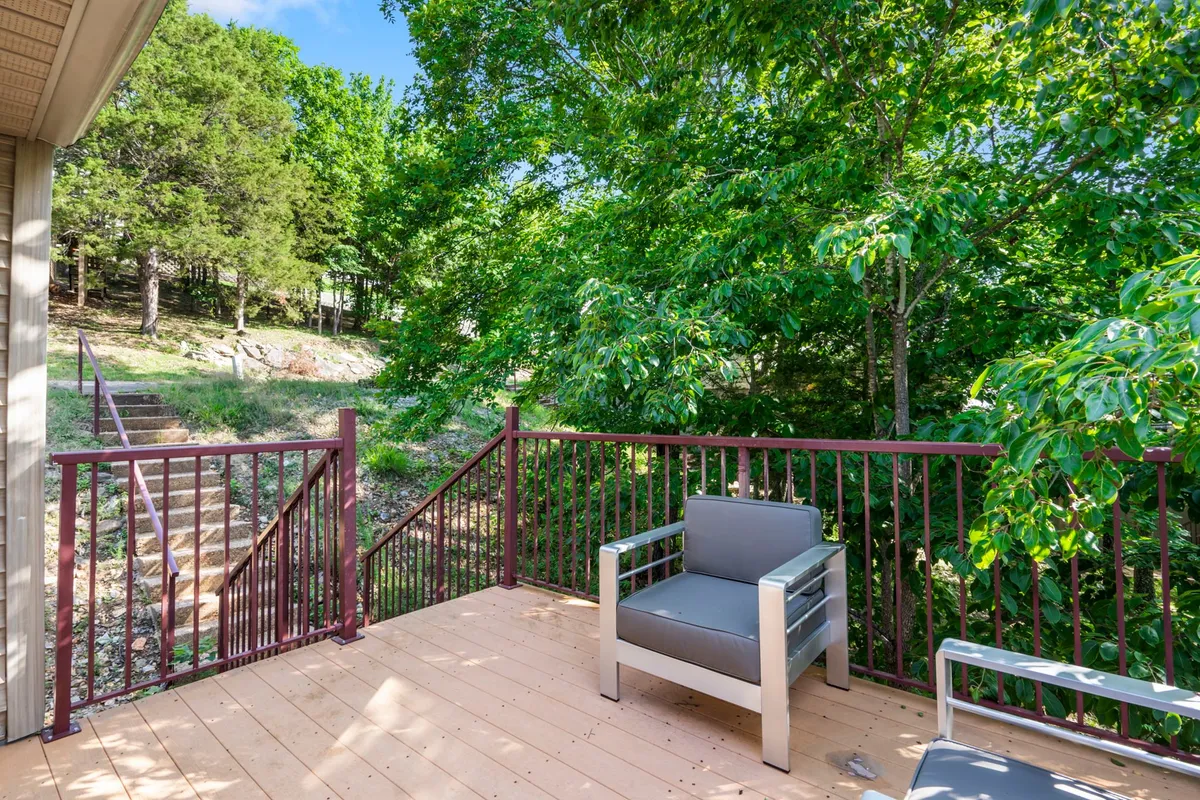 A wooden deck furnished with a comfortable gray armchair, surrounded by vibrant greenery. The space feels inviting and seamlessly connects the living area to the outdoors, ideal for relaxing after exploring with pets.