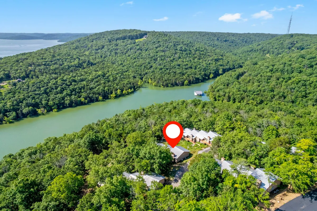 A tranquil river scene with the water flowing past lush forest and residential buildings. The view suggests opportunities for boating, hiking, and peaceful nature observation, with soft lighting hinting at early morning or dusk.