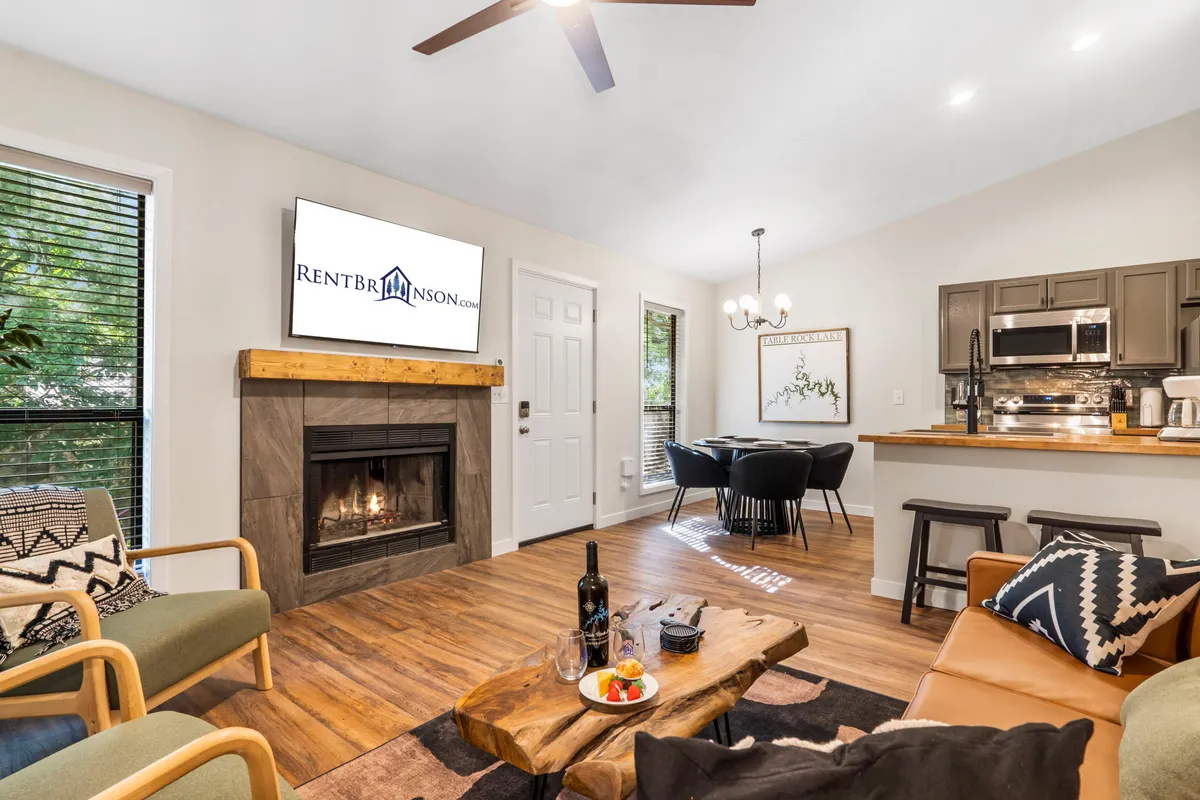 A cozy living area with a fireplace, wooden coffee table, wine and snacks, and a television. Soft natural light filters into the space, and the arrangement of comfortable seating invites relaxation and social time.