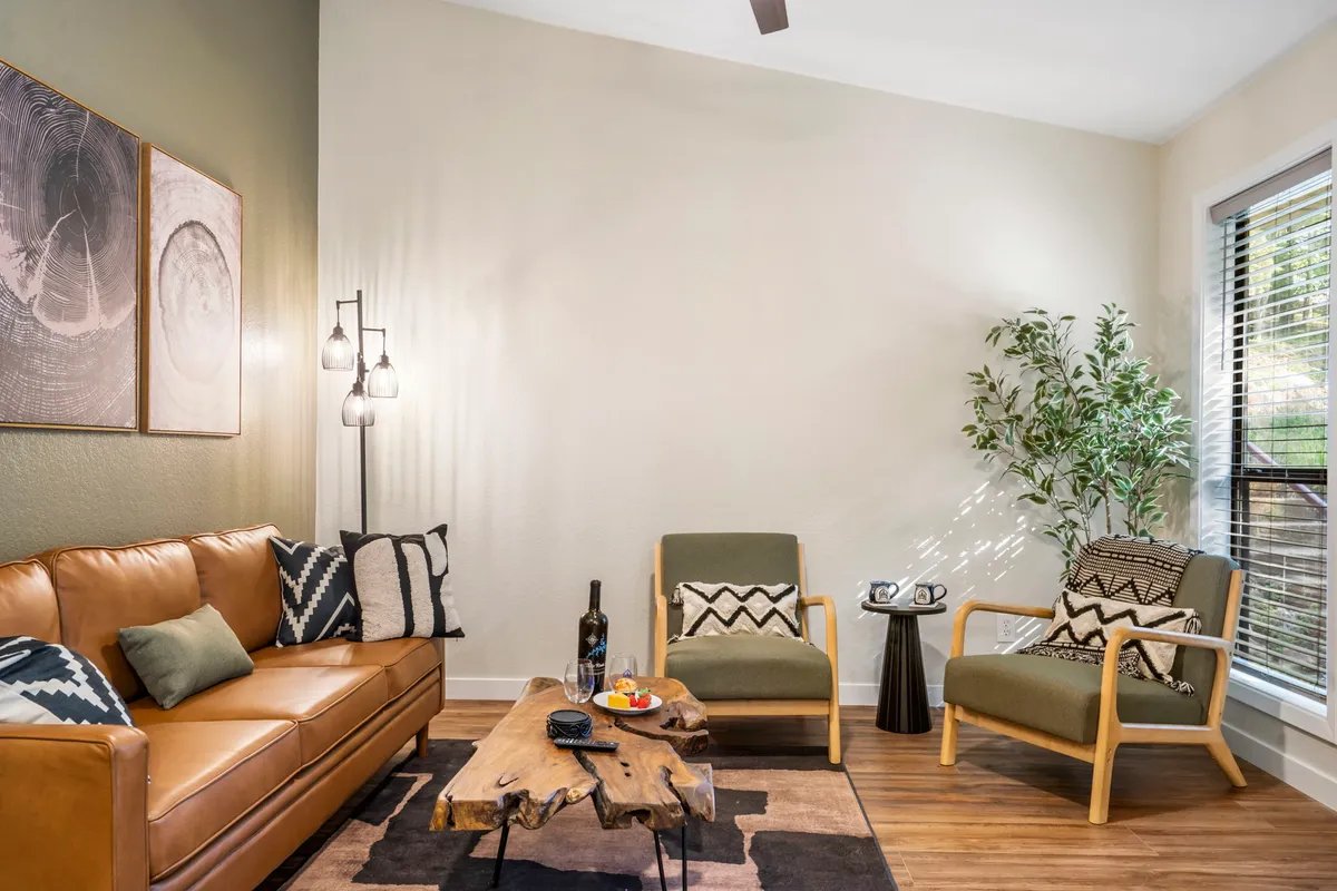A comfortable and stylish living area featuring a brown leather sofa, green armchairs, a wooden coffee table, and wall art. The space is accented with an indoor plant, creating a warm and inviting atmosphere.