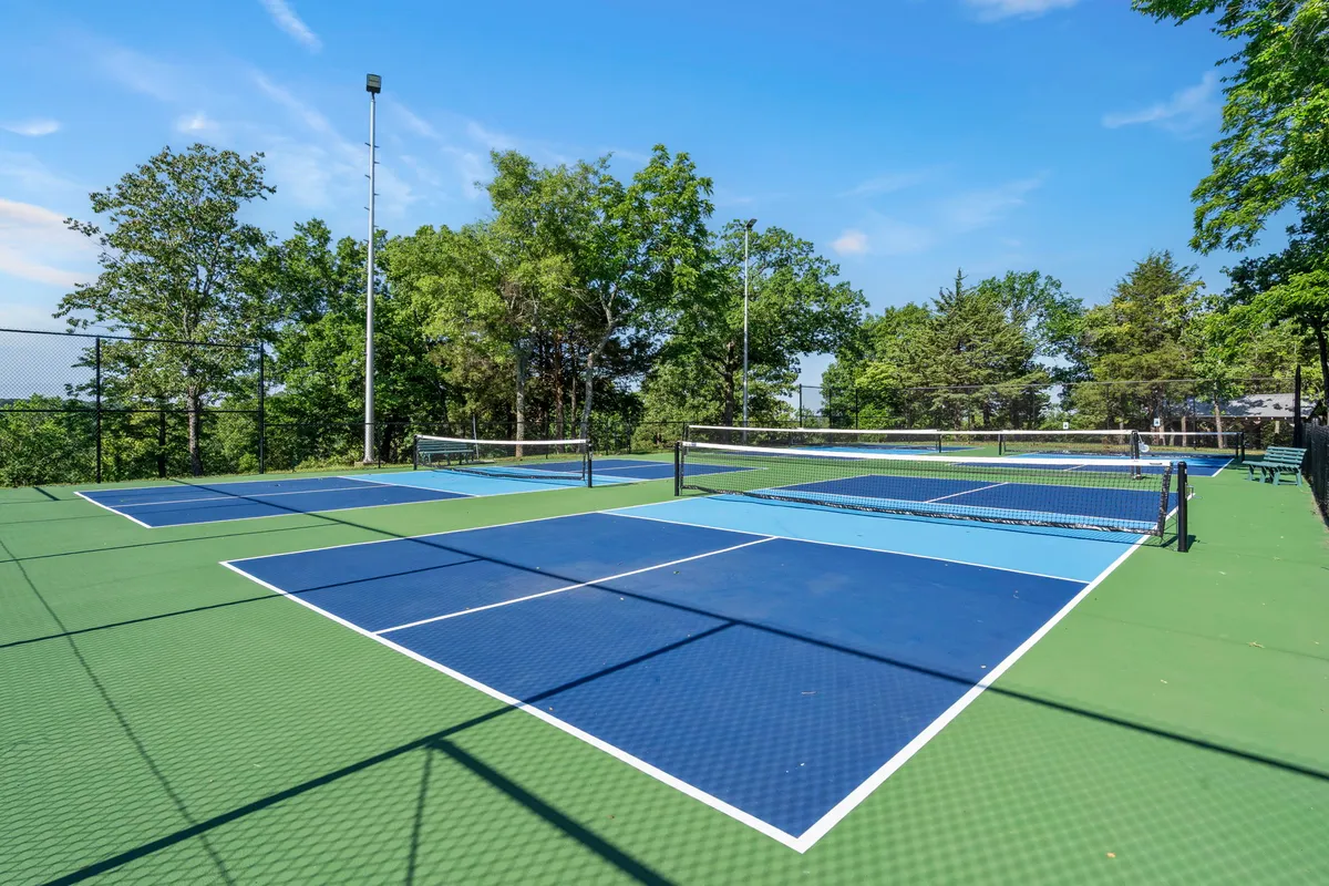 Well-maintained tennis courts stretch under a vivid blue sky and are surrounded by lush greenery, offering an energetic spot for guests to serve up a game or join in on community sports.