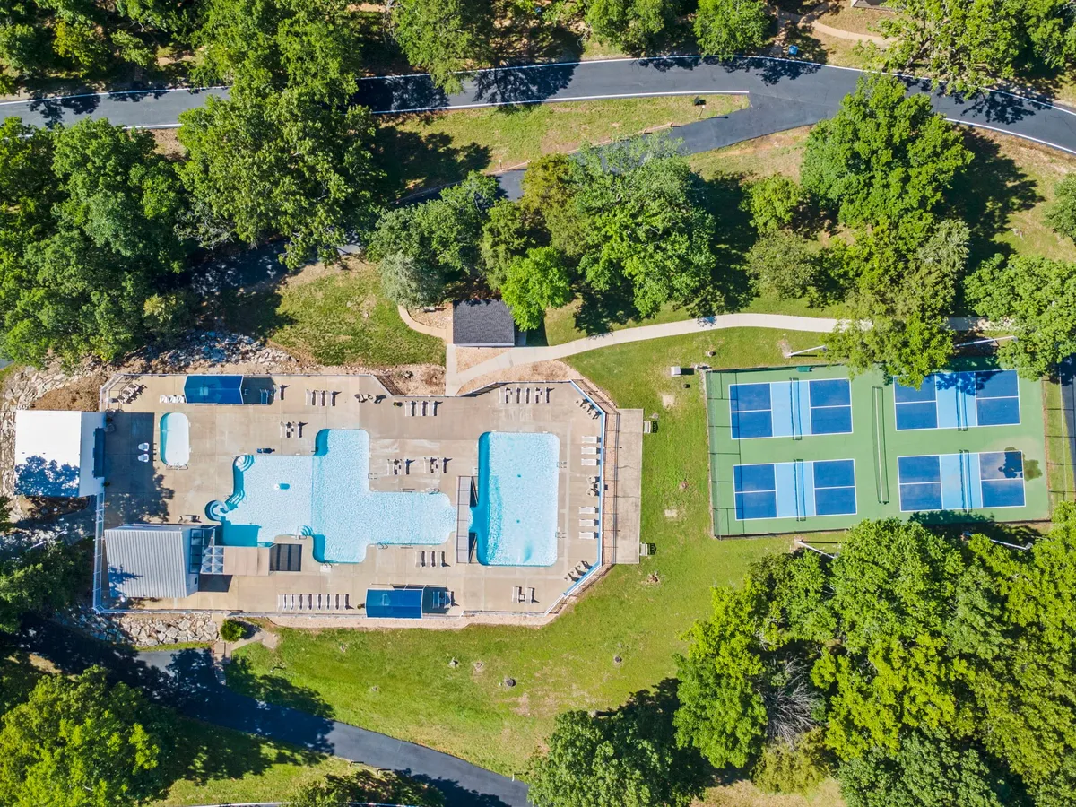 A vibrant scene featuring swimming pools, tennis courts, lounge chairs, and abundant greenery. The setting suggests resort-style amenities and a variety of recreational activities, ideal for active groups or families seeking adventure and relaxation.
