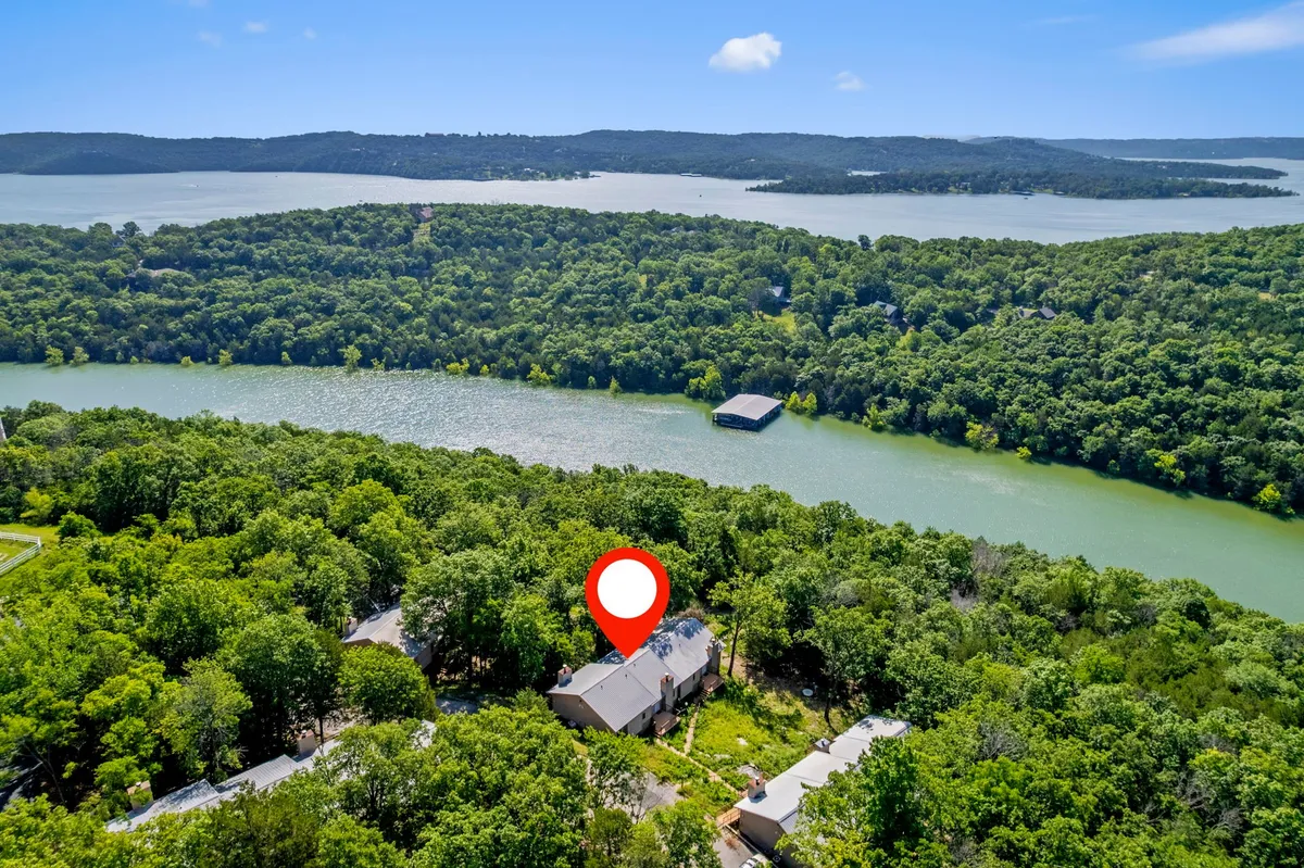 A panoramic view featuring lush greenery, sparkling water, the main house, and rolling hills in the distance. The expansive natural landscape suggests a variety of outdoor activities and family adventures.