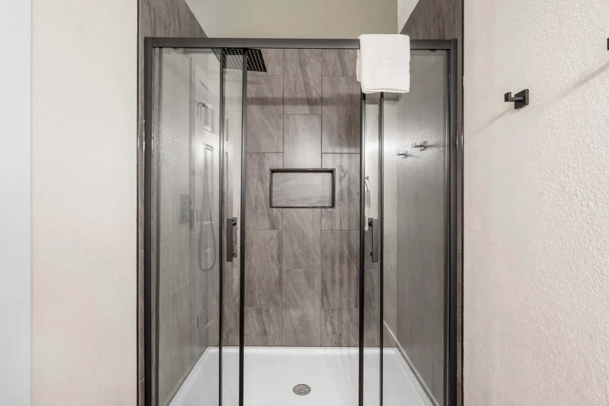 A modern bathroom featuring a glass shower enclosure, rainfall showerhead, and textured wall tiles. The clean, contemporary design emphasizes comfort and relaxation, offering an inviting space for rejuvenation.