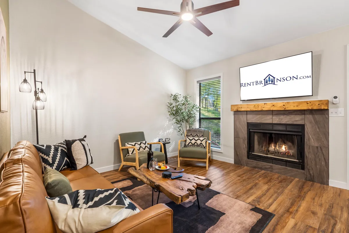 A cozy living room setting with a leather sofa, fireplace, wooden coffee table, and television. The space feels warm and welcoming, ideal for relaxing by the fire during movie or game nights.