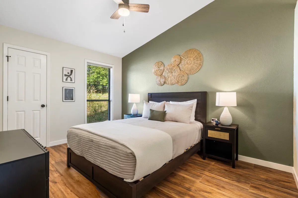 A tranquil bedroom featuring a plush bed, tasteful wall decor, nightstands with lamps, and a window that brings in natural light. The serene color palette and simple, clean lines create a calm and restful atmosphere, ideal for relaxation after a day of activities.